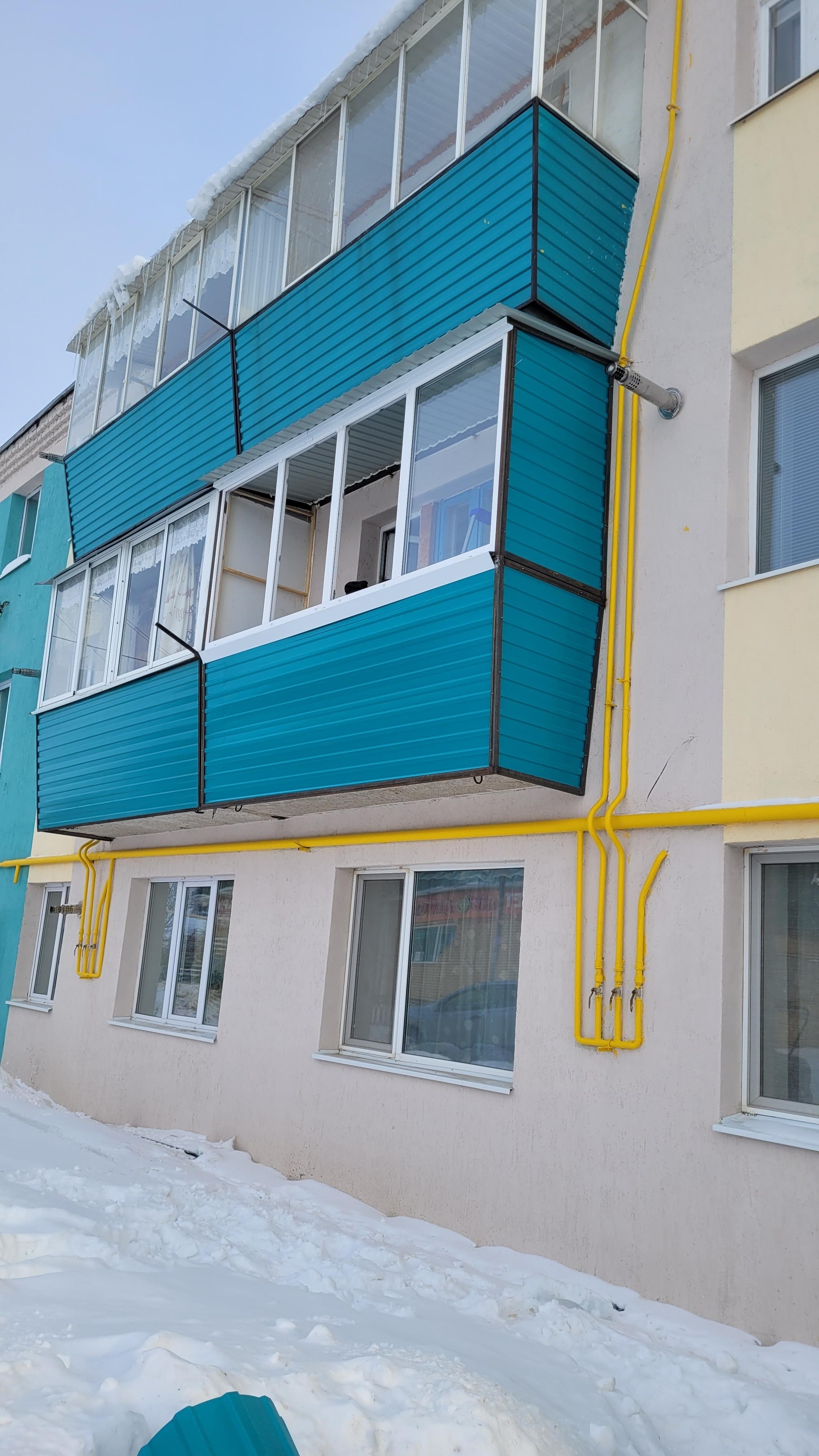 Остеклённые балконы с бирюзовой отделкой на фасаде.