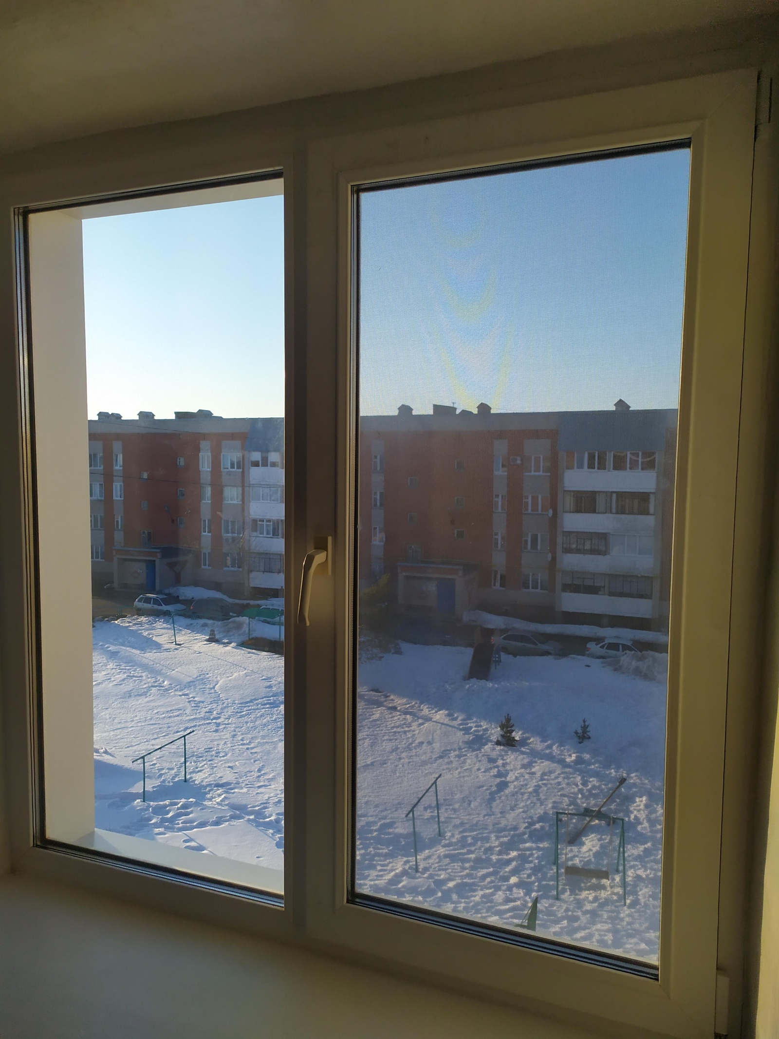 Двухстворчатое окно с видом на заснеженный двор.