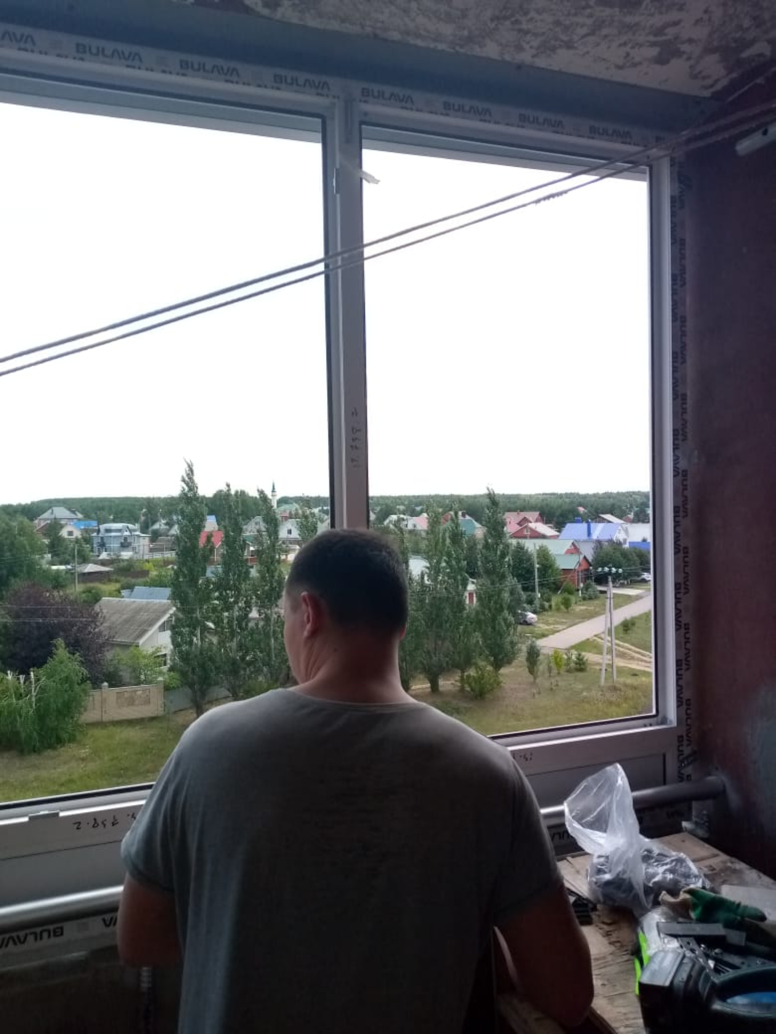 Человек у окна на балконе с незавершённой отделкой.